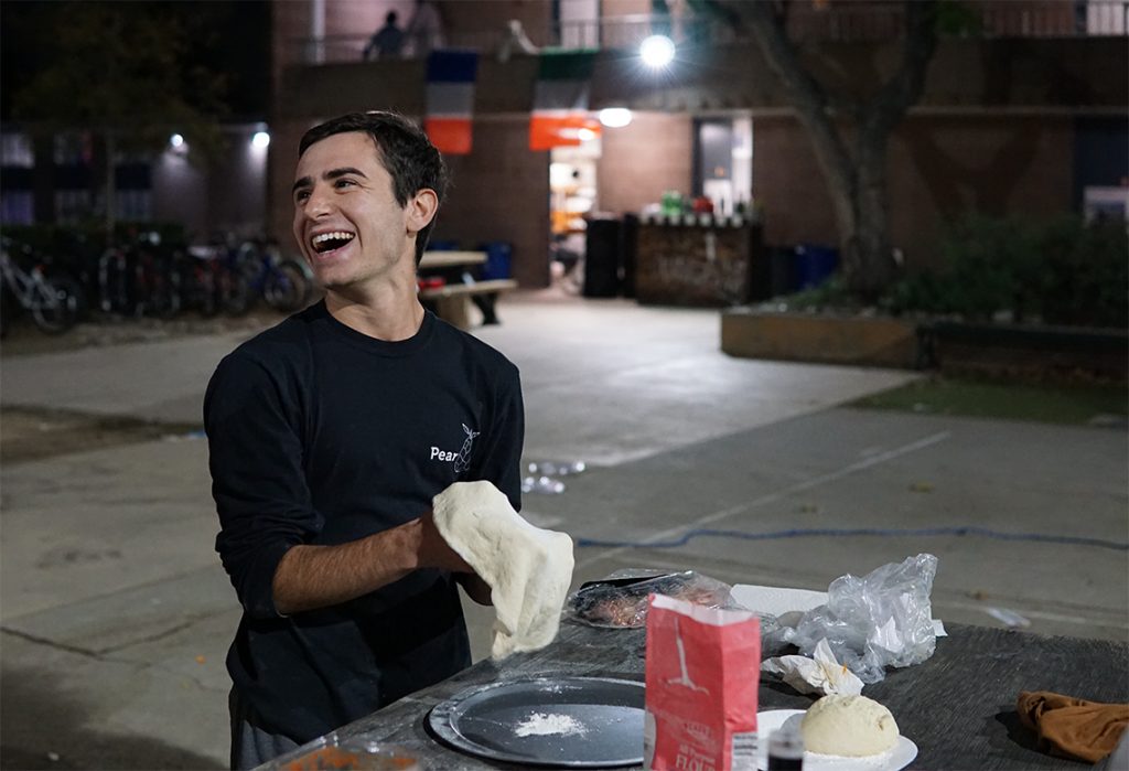 A laughing student prepares dough in an outside setting.