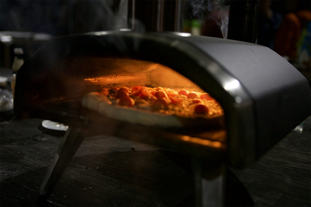 A pizza cooks in an outdoor pizza oven.