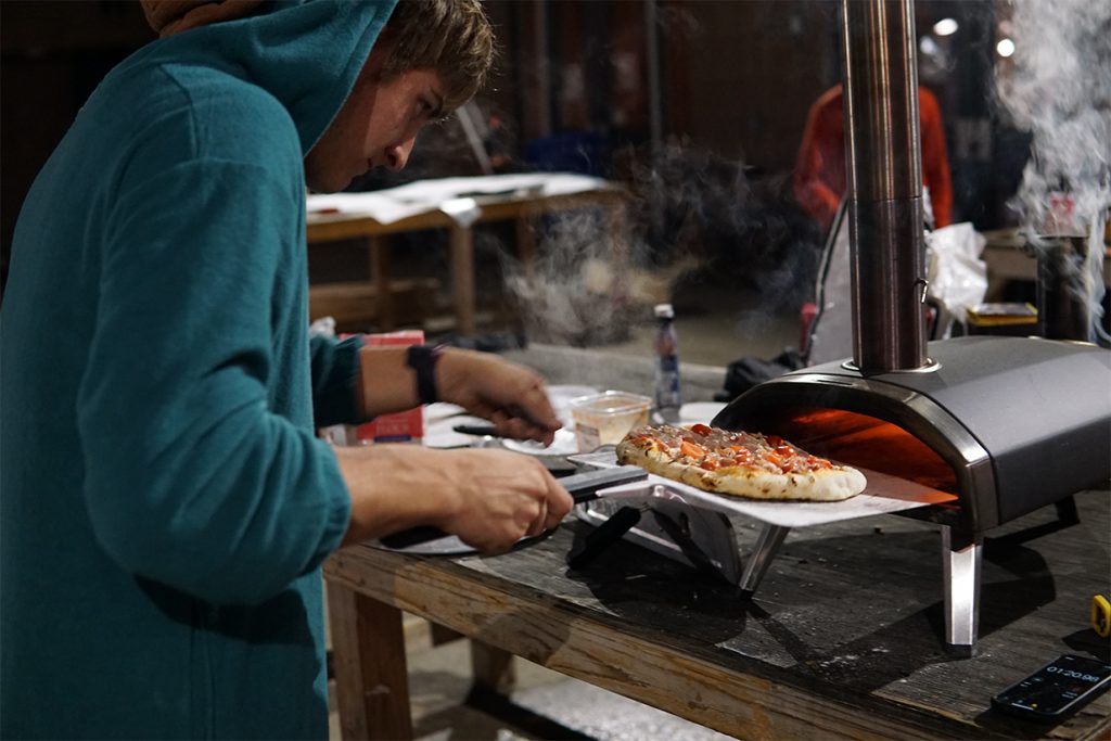 A student prepares to insert a pizza in an outdoor pizza oven.