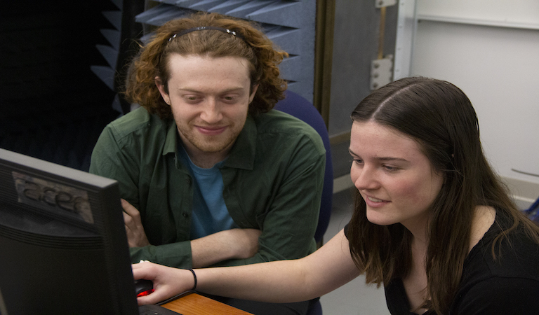Students sit side by side smiling and looking at a computer screen.