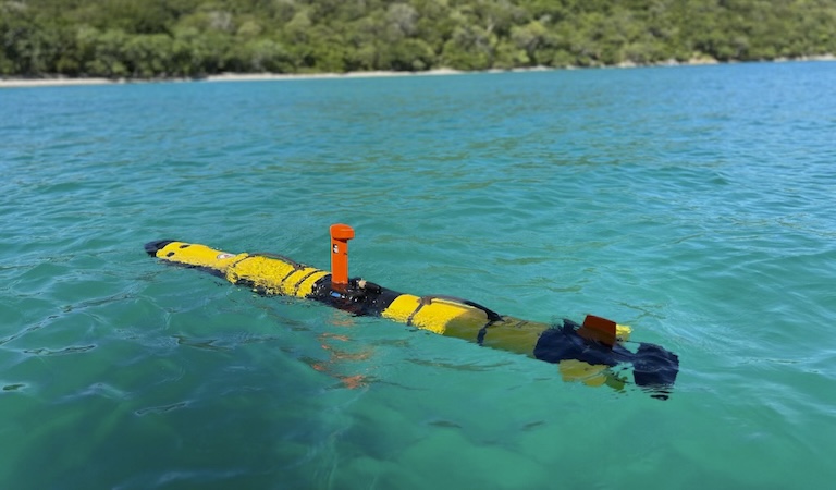 The yellow, cylindrical IVER3-AUV floats in clear blue-green water.