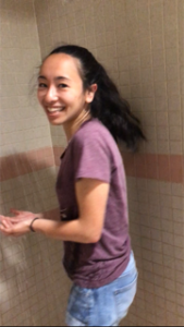 Anya stands fully clothed in a shower stall