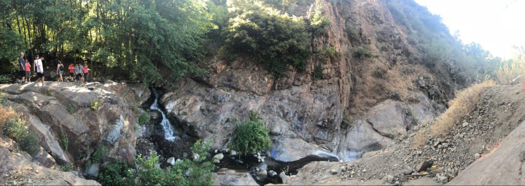A panorama of a small waterfall and a rocky hillside.
