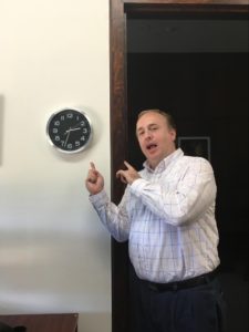 A photograph of Paul Hardister pointing to a clock.