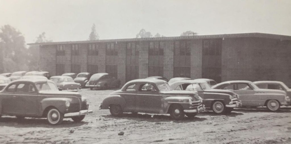 Cars parked on a dirt lot in front of a concrete building