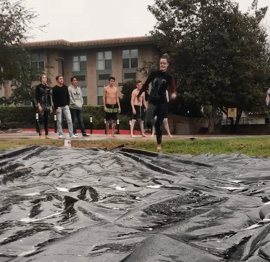 A girl in a wet suit sitting into a tarp in the rain.