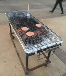 This picture shows that a metal grilling surface has been put over the coals, so that there's something to put the patties on. There are 3 relatively raw patties on the grill.