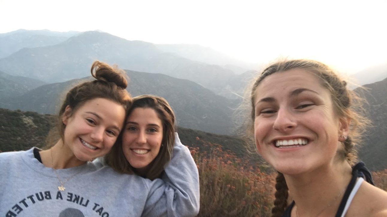 A selfie of three girls smiling in front of a range of mountains.