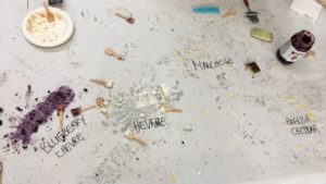 Pictured is a top-down view of a big piece of paper with spoons and various types of cheese strewn about.