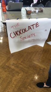 A poster with the words 'The Chocolate Society' is hanging off a table.