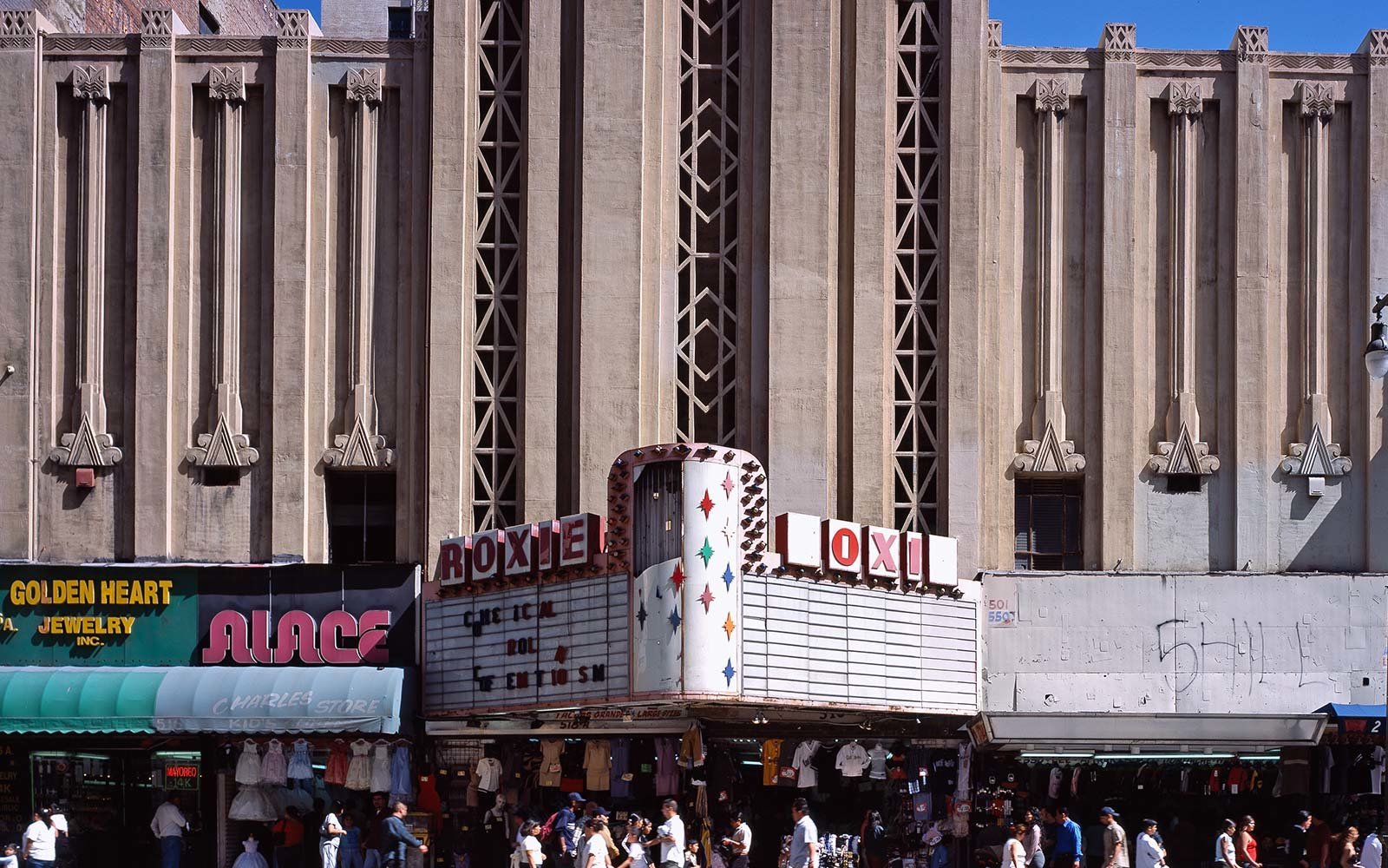 The exterior of the Roxie theater is an art deco style. Lots of people are walking around, and the first floor units have turned into local merchant booths