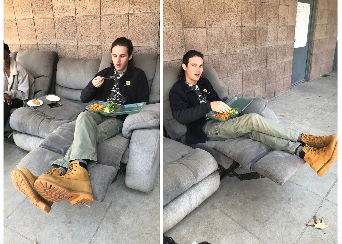 Bradley is wearing a black clinic fleece, green pants, and yellow-brown work boots. He is sitting on a couch and eating out of his green box