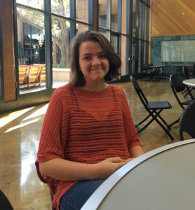 A picture of Marz sitting in a chair, wearing a red top.