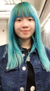 The picture is a selfie of Shanni. She is wearing a jean jacket, and has blue, dyed hair.