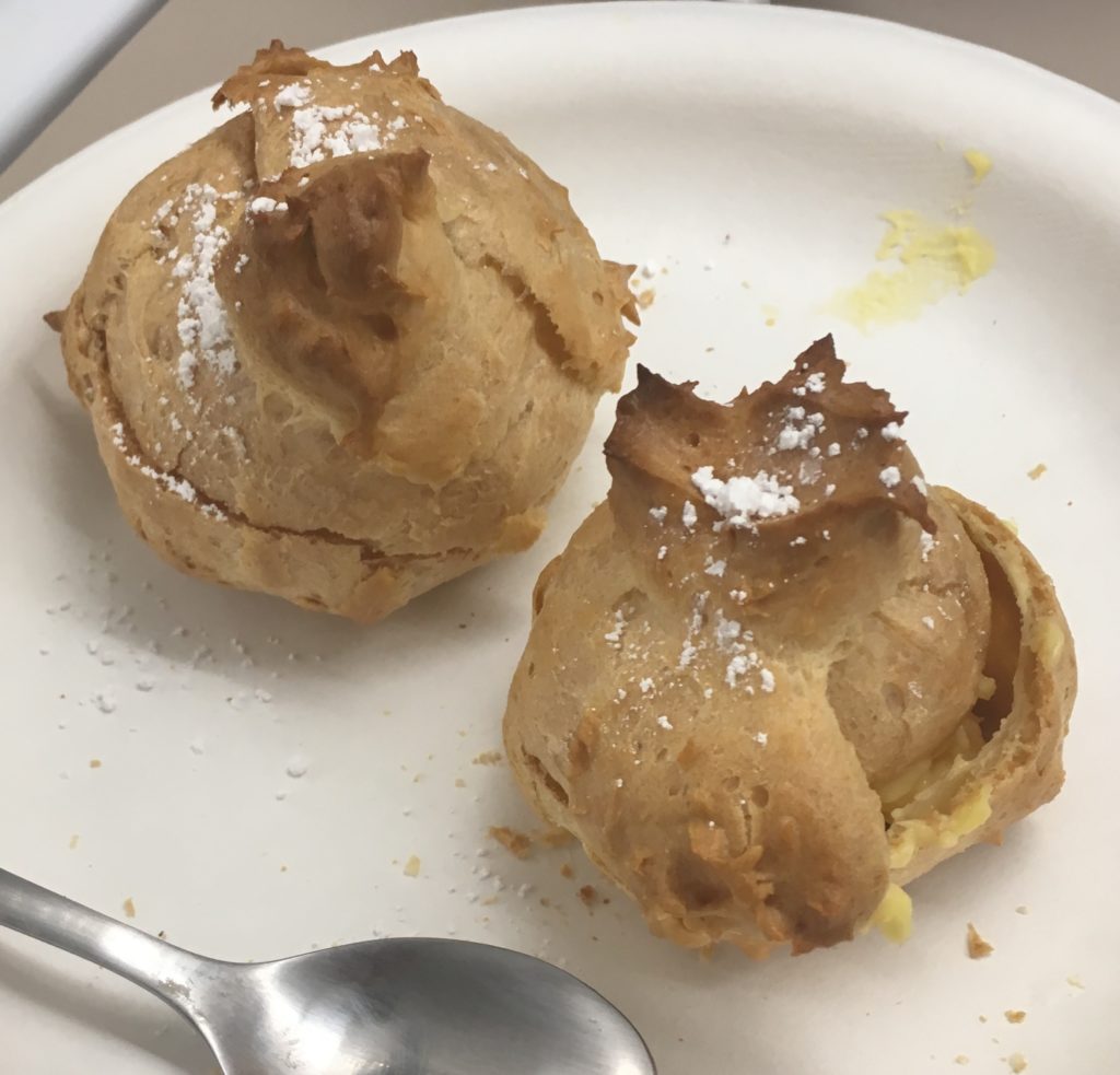 Two perfect cream puffs, topped with powdered sugar and filled with custard