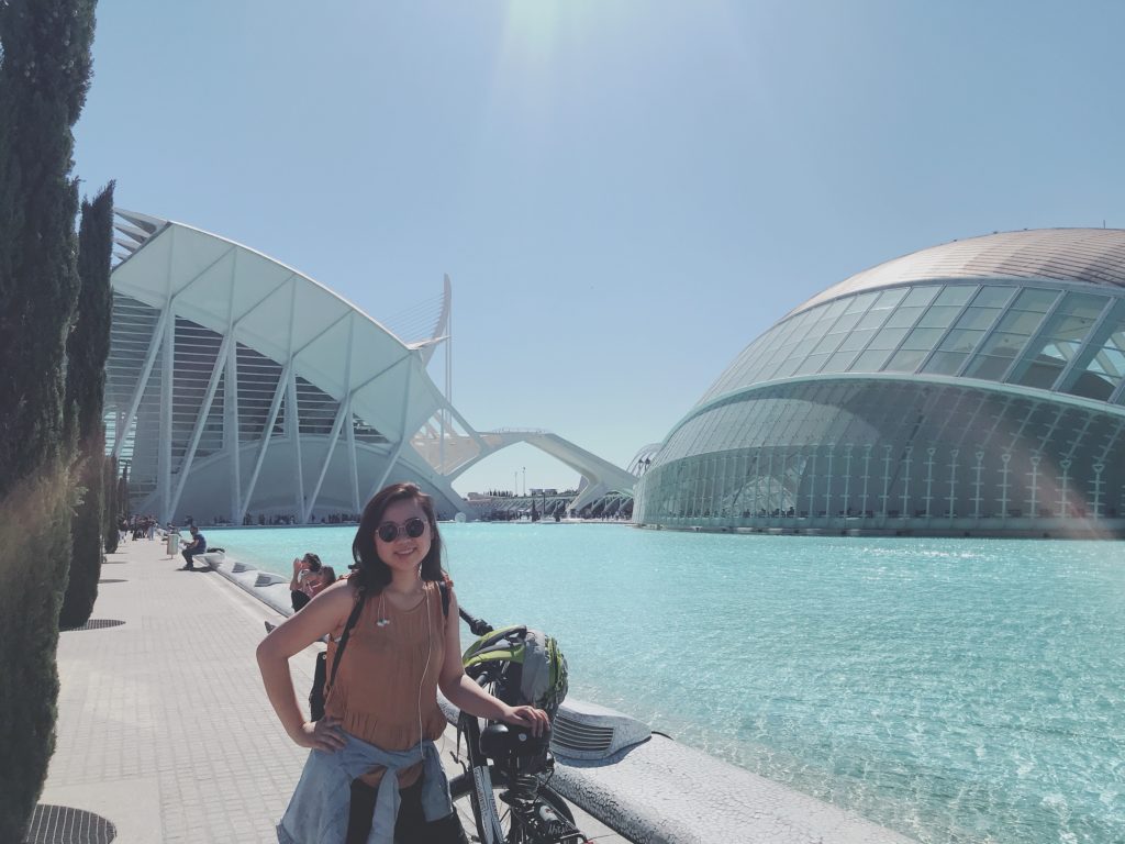 Jasmine and her bike in front of a pool and right, wind buildings