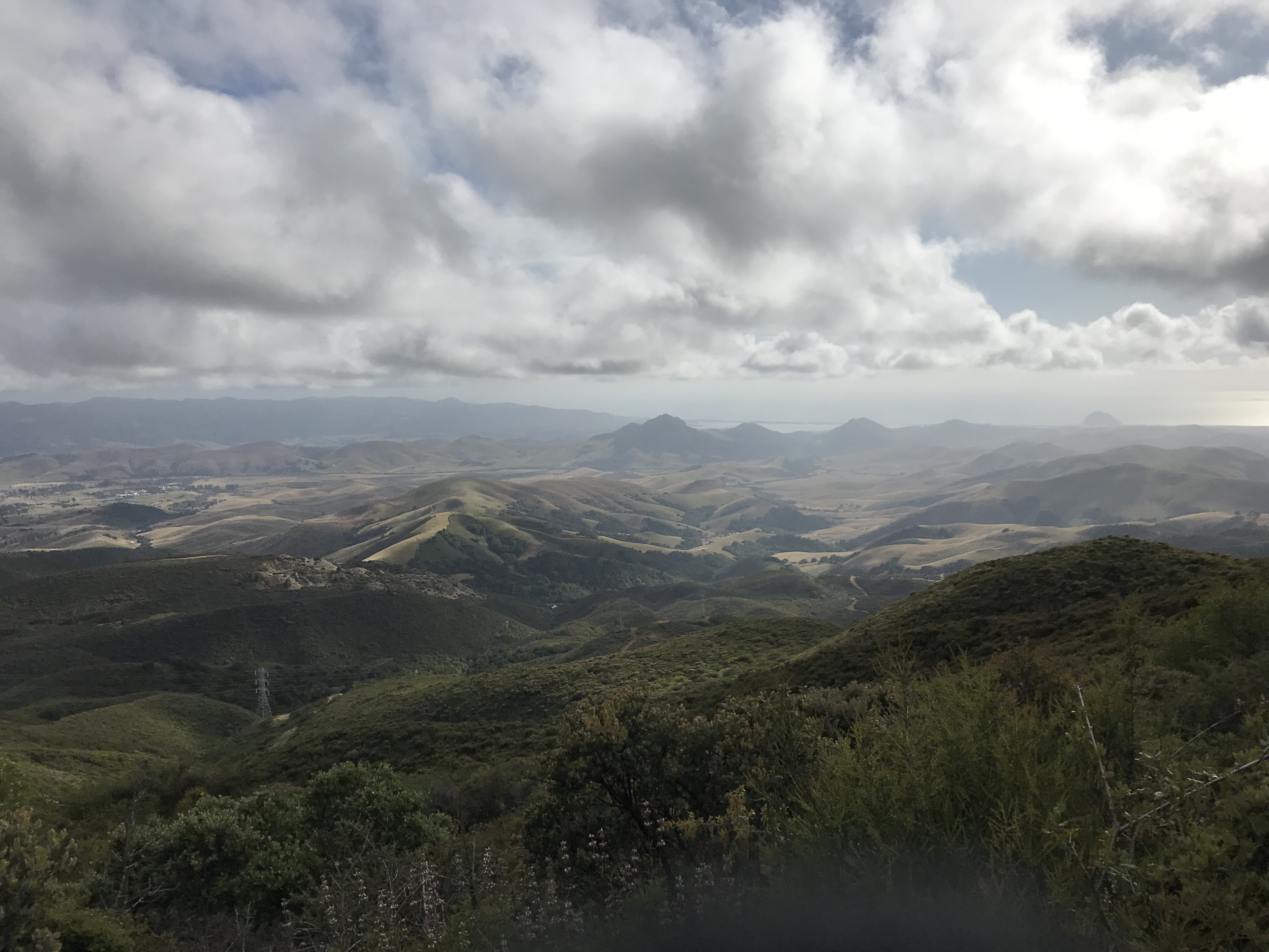A view during the drive up to Pismo Beach. The clouds are low and there are lots of rolling hills. The landscape is darkened due to the cloudy sky.