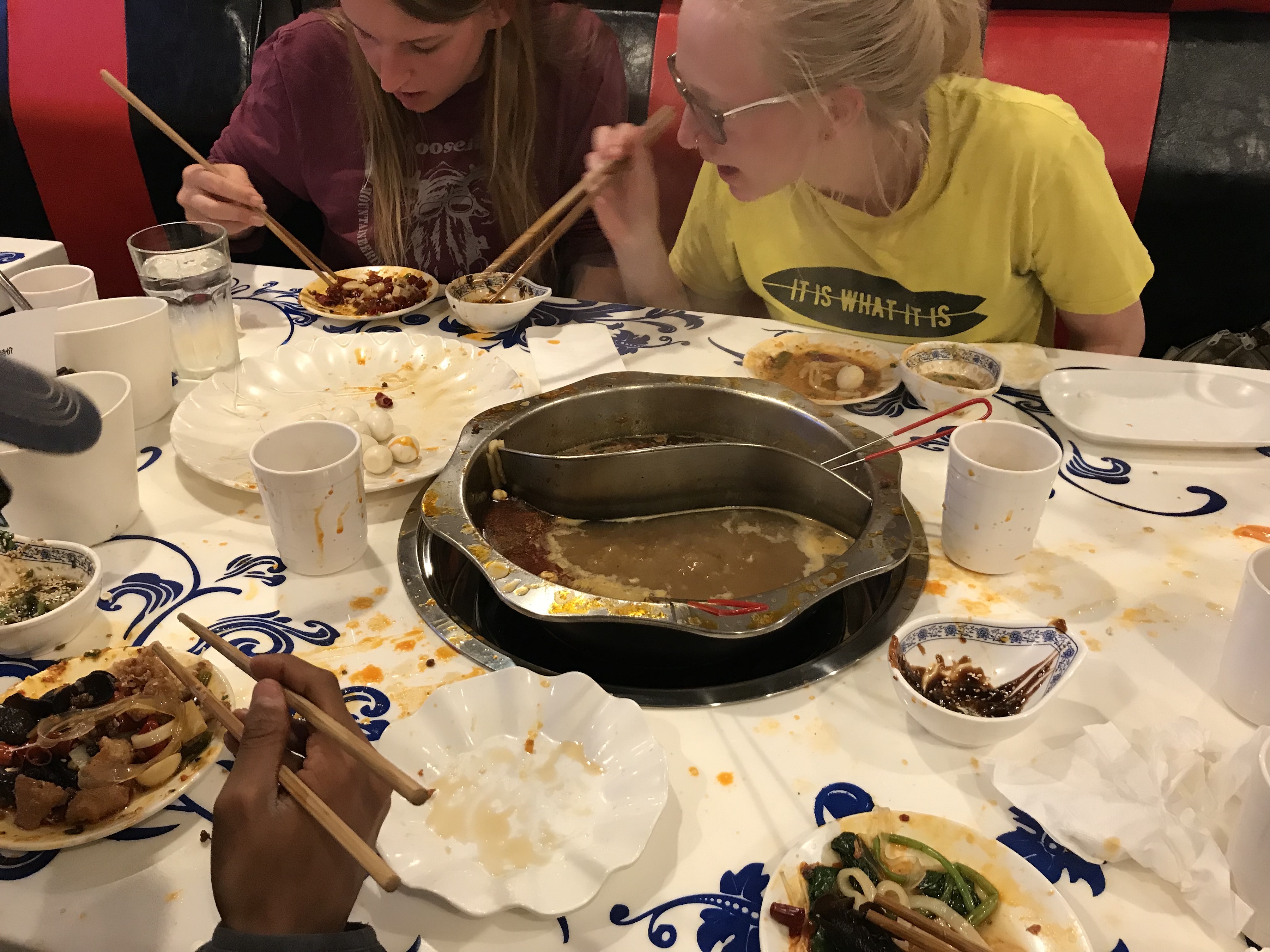 There are several plates on our table at the hot pot restaurant. My friends are picking up their food to eat from the broth.