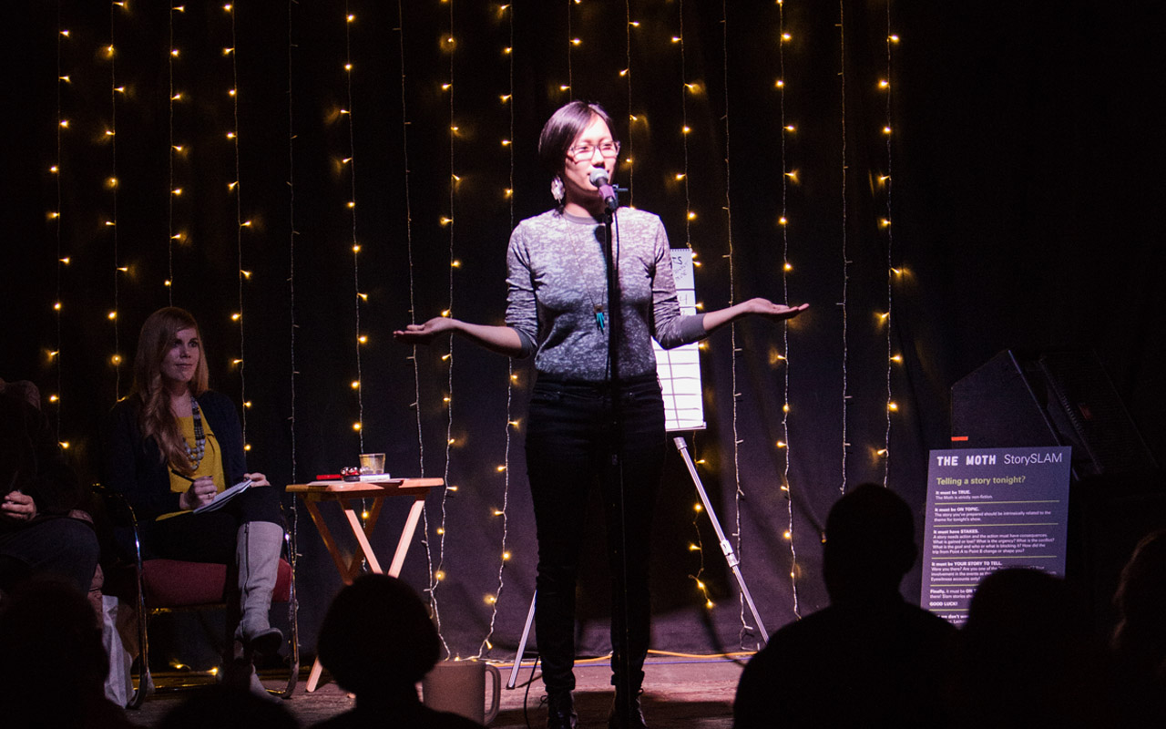 A storyteller stands on stage with her arms stretched out, engaged in her story