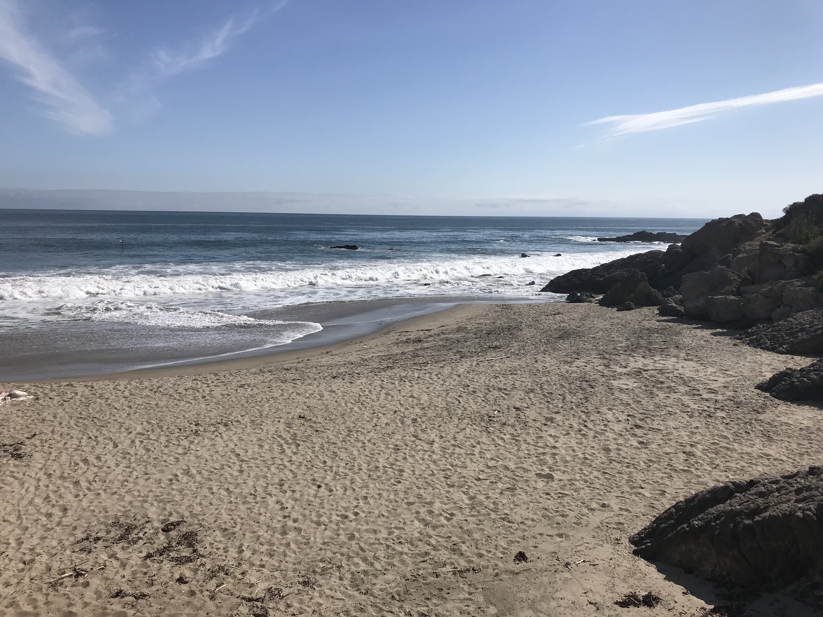 A picture of the cove at Leo Carrillo state park. A sandy beach cove is bordered on the right by rocks, while on the left there is a calm shoreline.