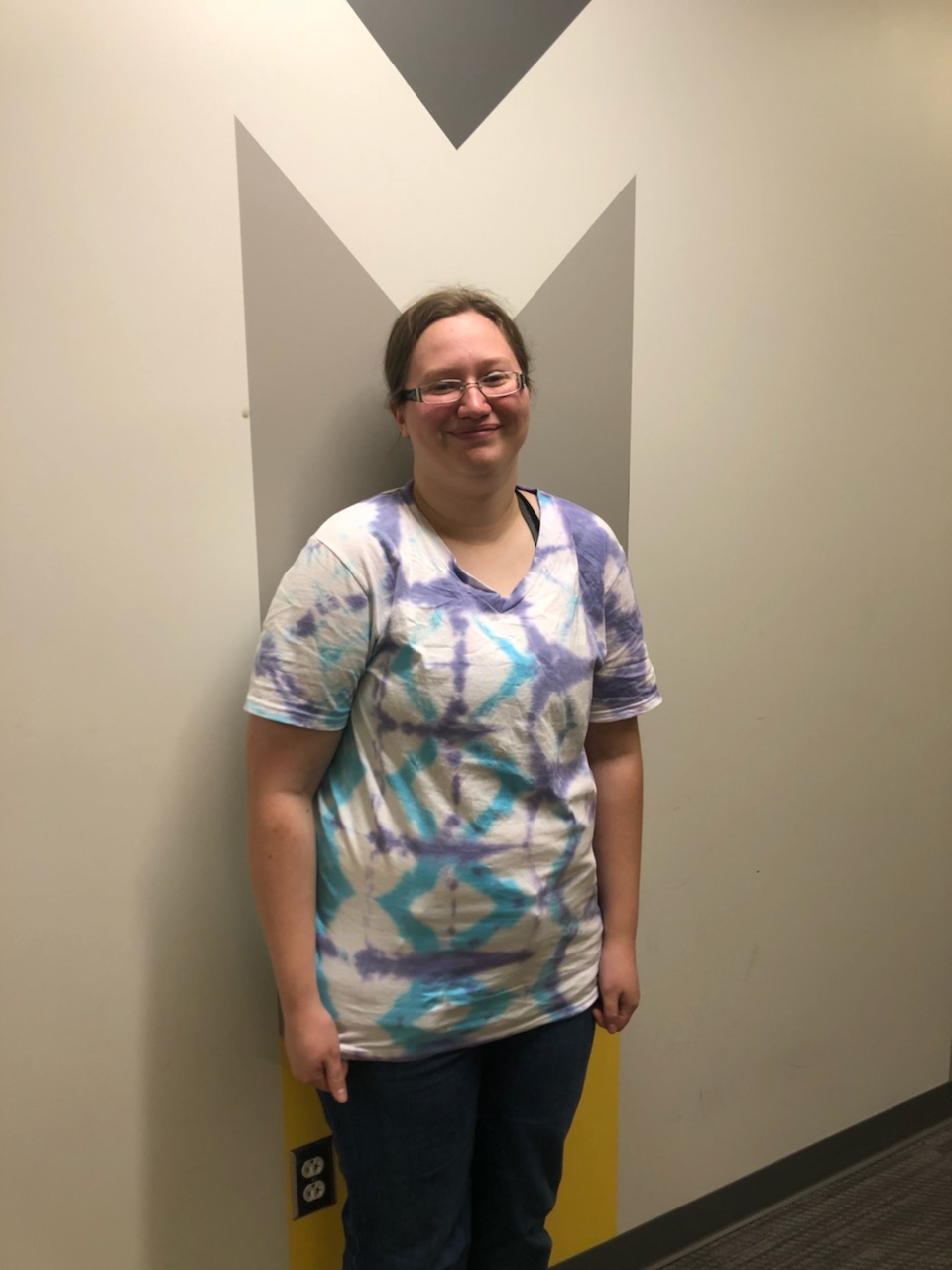 Anya wears a white t-shirt with a crisscrossing purple and light blue diamond shape.