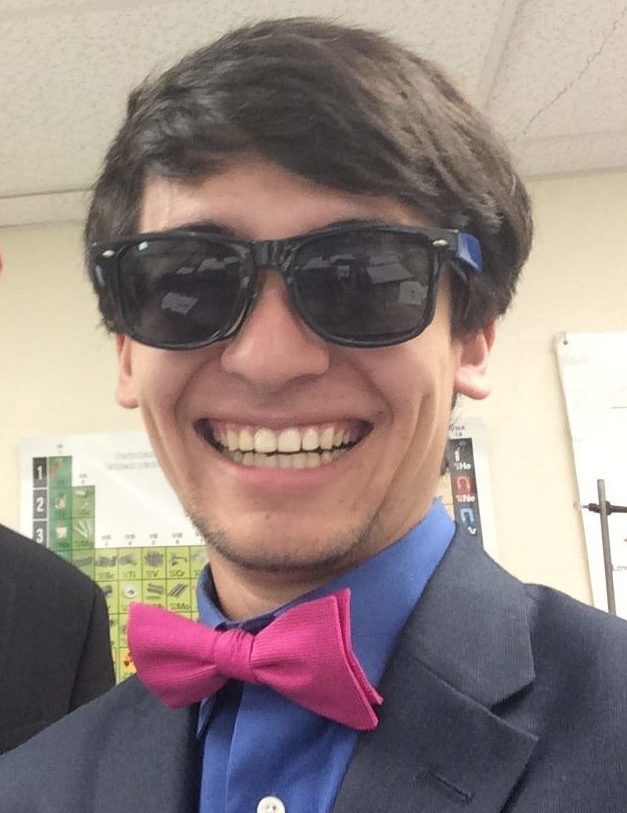 Joaquin, wearing a bowtie, sunglasses and a suit, with his high school hairstyle. His black hair sweeps over his forehead, leaving some of it exposed. Very little effort necessary for maintaining this haircut