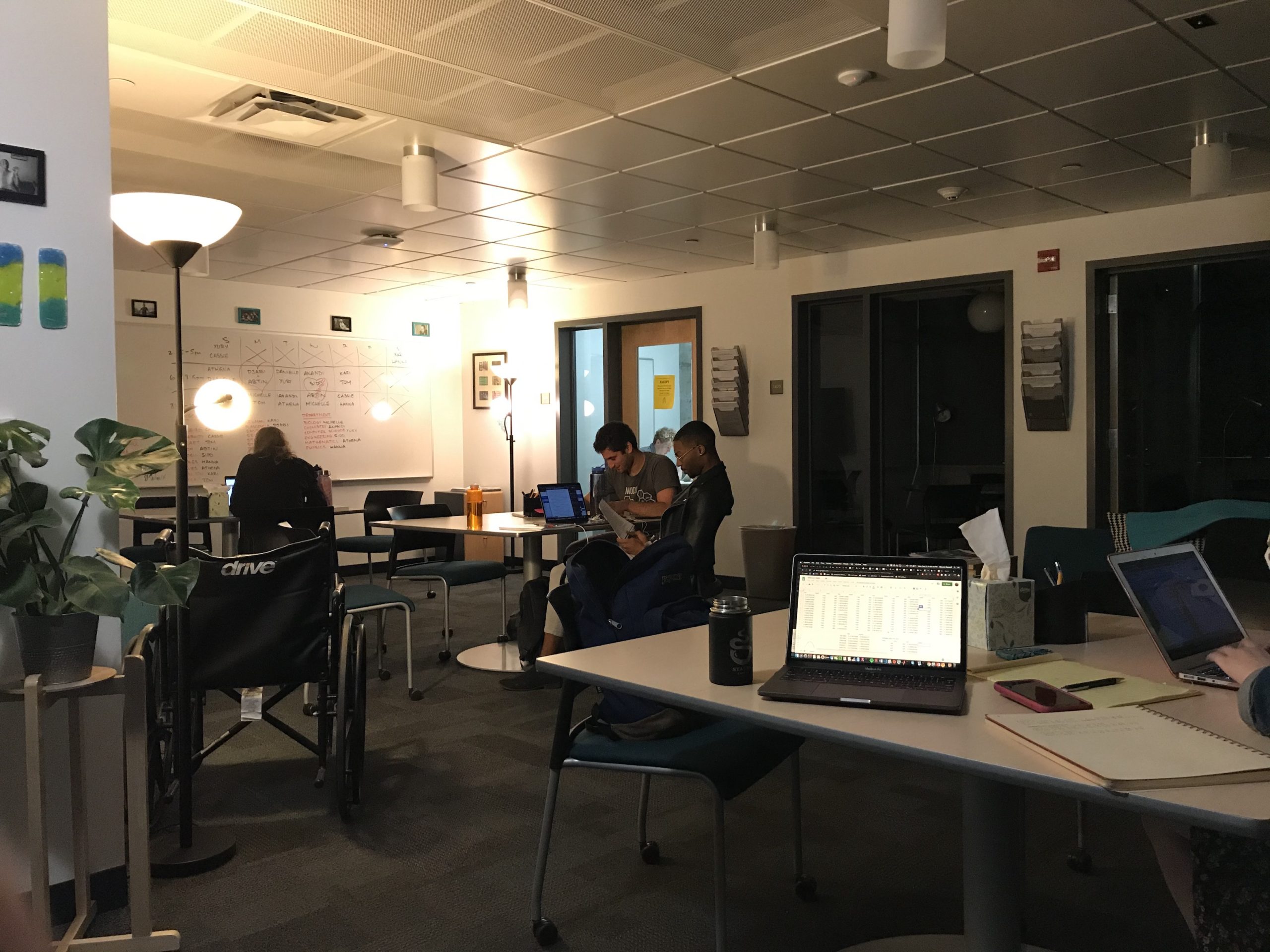 Students work at the collaborative tables in the Writing Center. In one of the private rooms, a student consultant is helping another student with their writing.