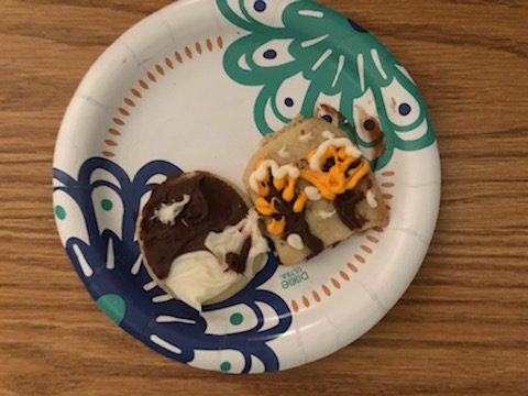 Two decorated cookies on a plate, one with autumn trees and one with a geometric brown and white design.