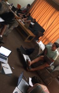 About 6 students in a common room surrounded by laptops and notebooks.