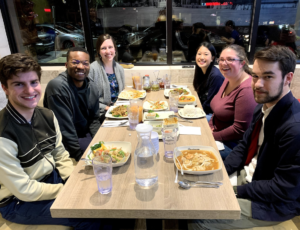 Hannah, Kailee, and three other college students sit at a table with a professor. Thereâs lots of food on the table.