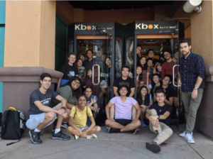 A large group of college students pose for a photo on a sidewalk outside