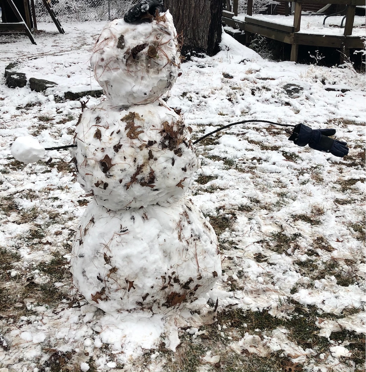 A snowman with leaves mixed into the snow.