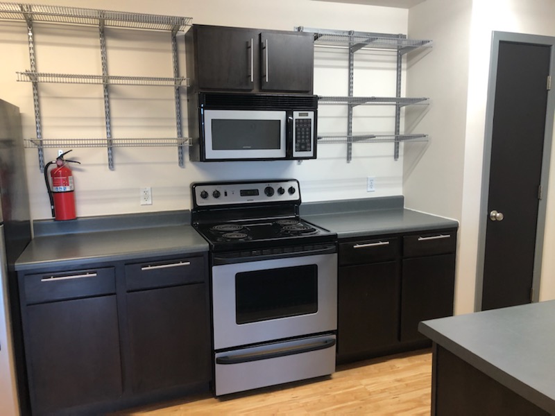 A kitchen with a stove and microwave. The counters and shelves are empty.
