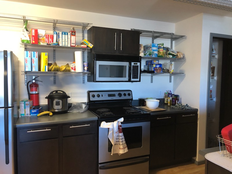 A kitchen with a stove and microwave. The counters and shelves are full.