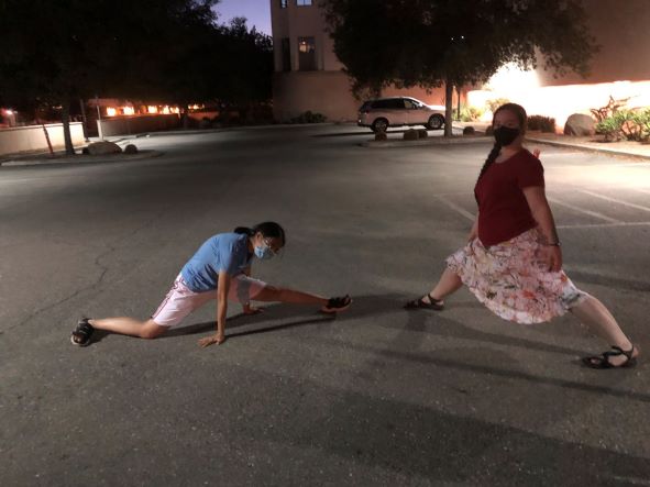 Two people doing the splits in a parking lot, one with much more success than the other. 