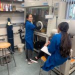 Emily and another student in lab coats next to a large piece of chemistry equipment