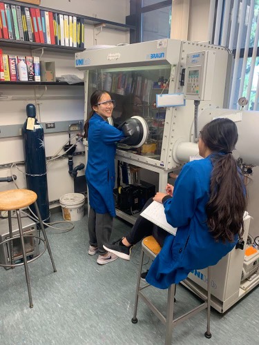 Emily and another student in lab coats next to a large piece of chemistry equipment