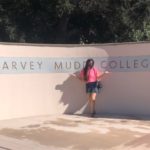 Ana in front of a white and blue sign that reads "Harvey Mudd College"