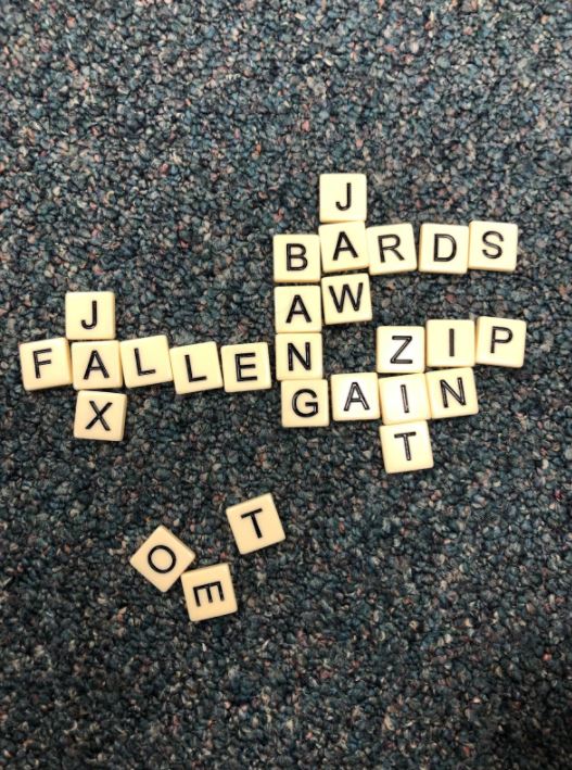 Bananagram tiles spelling out fallen, jax, bang, bards, jaw, zip, gain, aw, in, and zit interwoven to look like a crossword puzzle.