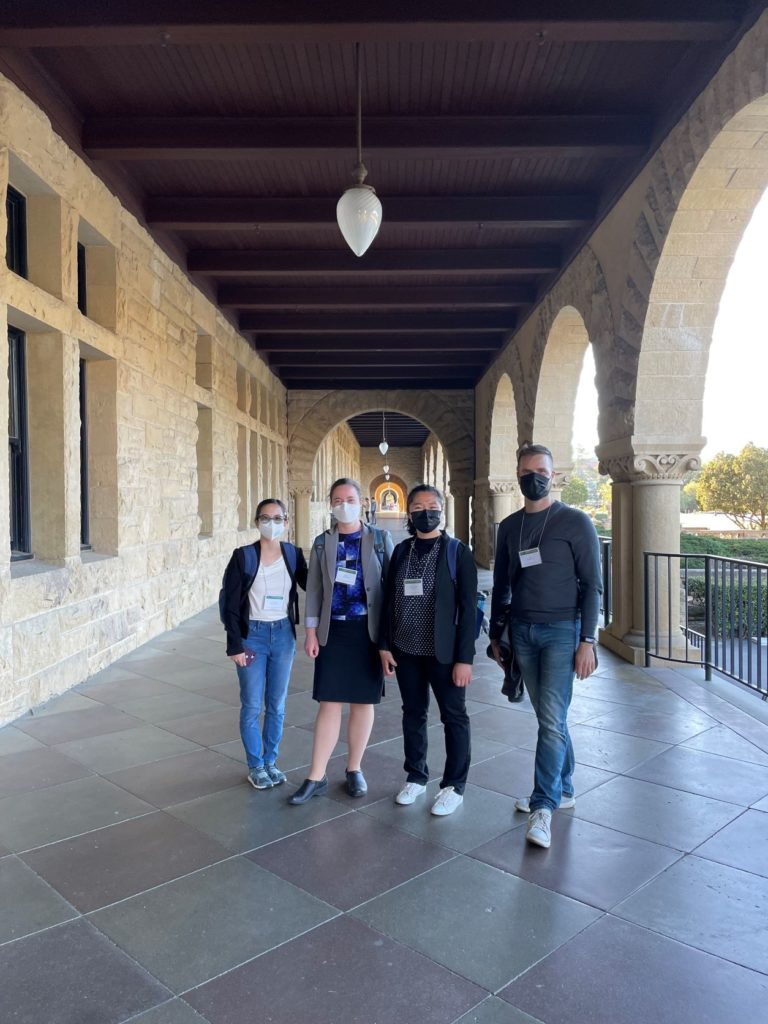 Three students and a professor standing in an outdoor hallway