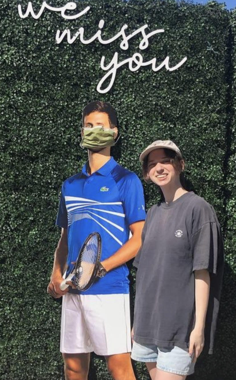 Laney posing with the cardboard cutout of a tennis player, underneath a sign that reads "we miss you"