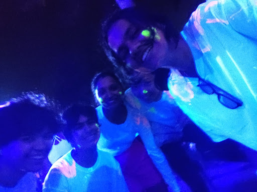 Five smiling people wearing white shirts with glowing paint on them