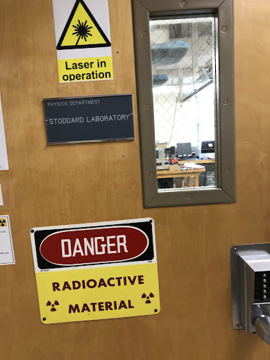 Signs on the door read "Laser in operation", "Physics Department: Stoddard Laboratory", and "Danger: Radioactive material"