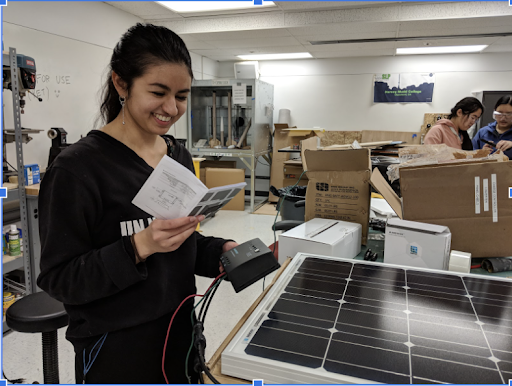 A smiling student reading a manual booklet with solar panels in front of her