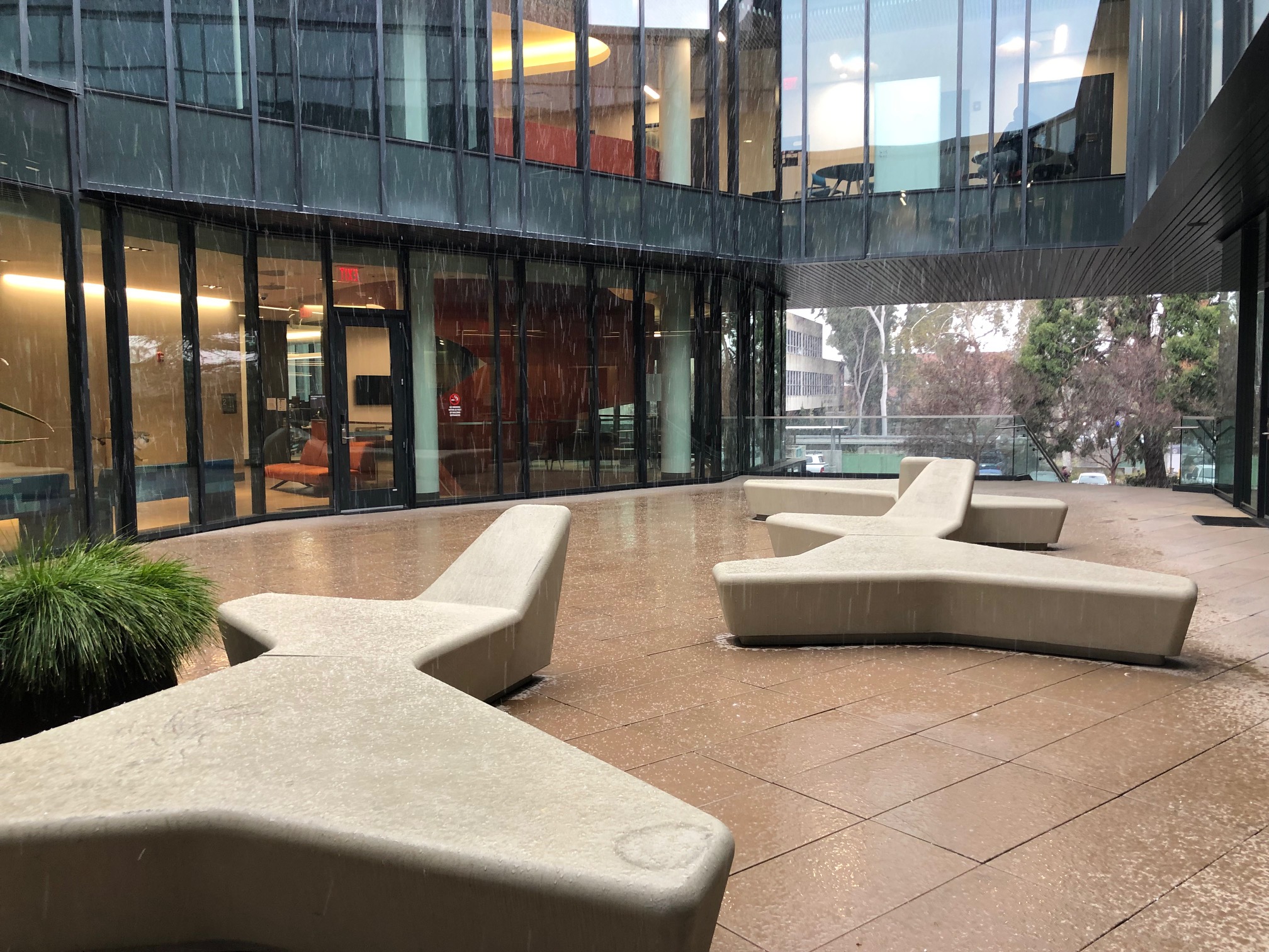 Several concrete benches along a courtyard with windowed walls behind them.