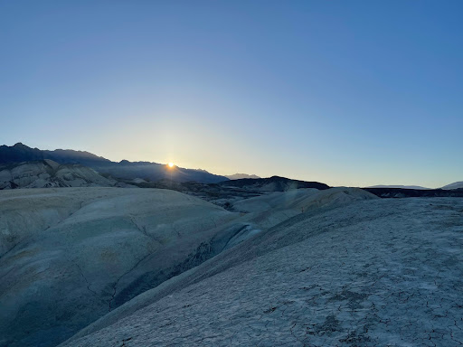 Barren hills and rock formations with the sun beginning to rise in the background