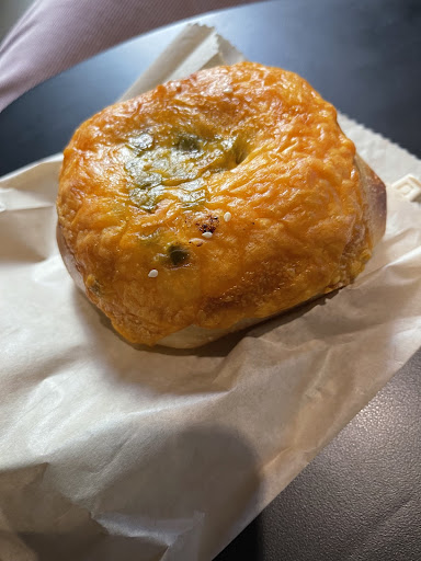A bagel covered with a layer of cheese over jalapeños on top of a brown paper bag