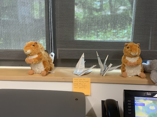 Two small stuffed animal squirrels on a shelf with paper birds in between them.