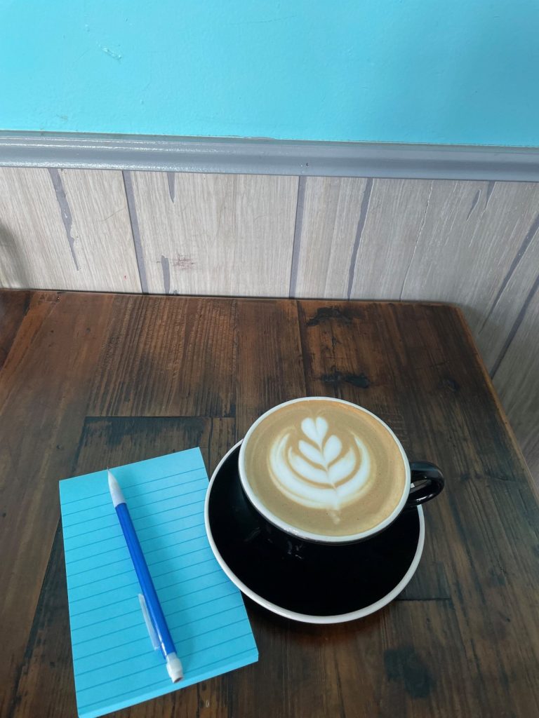 Drink in cup on table next to notepad and pen.