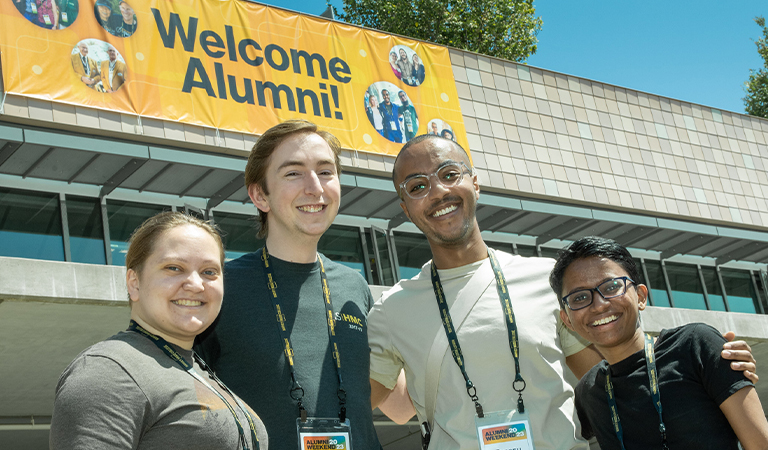 Harvey Mudd alumni pose in front of a banner.